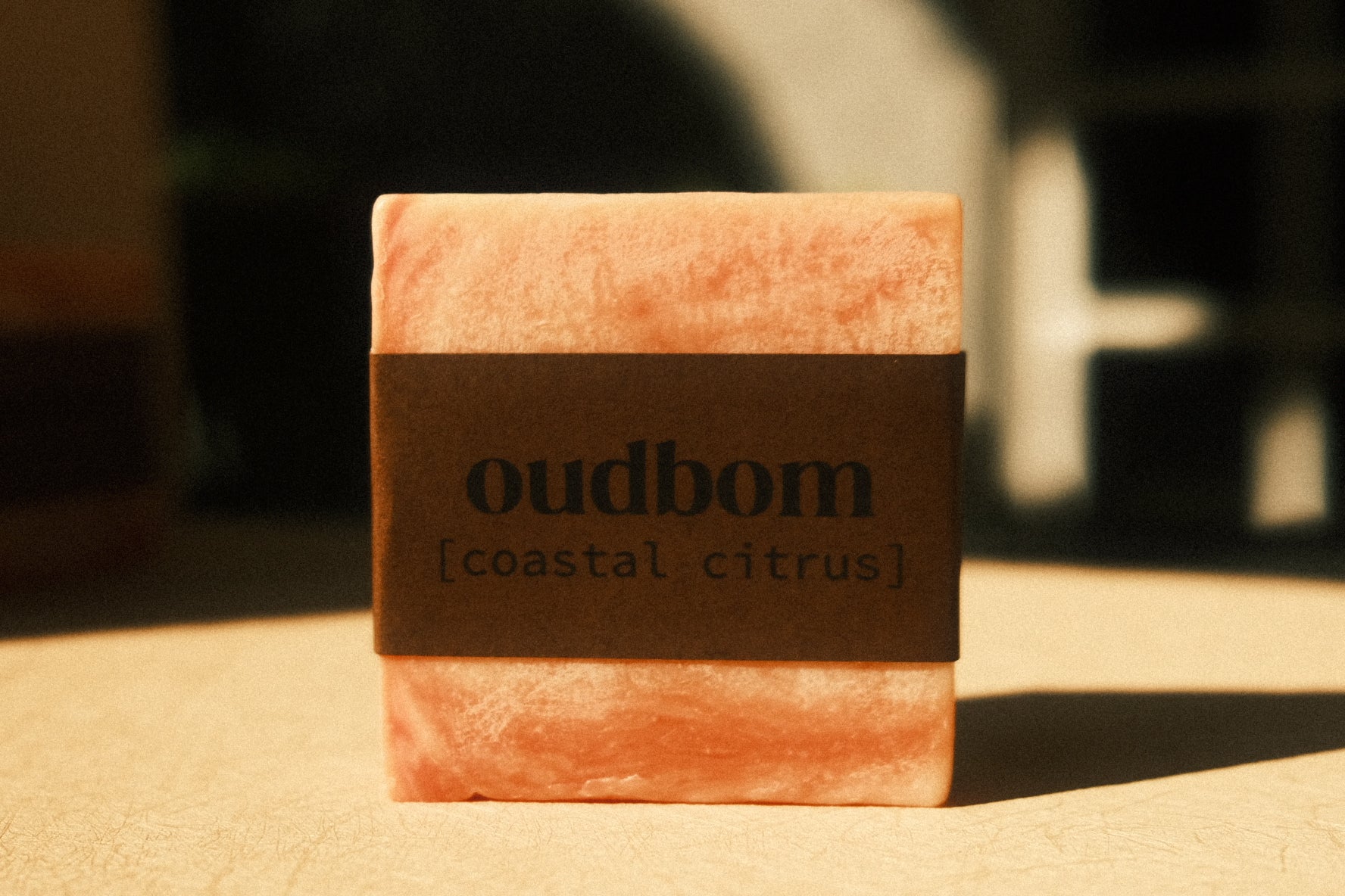 Bar of marbled orange soap with a brown label, “oudbom, coastal citrus”