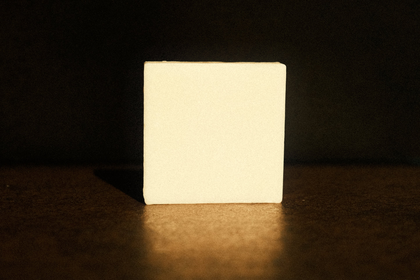 White bar of soap stands with brown floor and background, its reflection shining faintly underneath