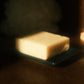 A white bar of soap on navy blue soap dish with a stack of cubes sitting in the background