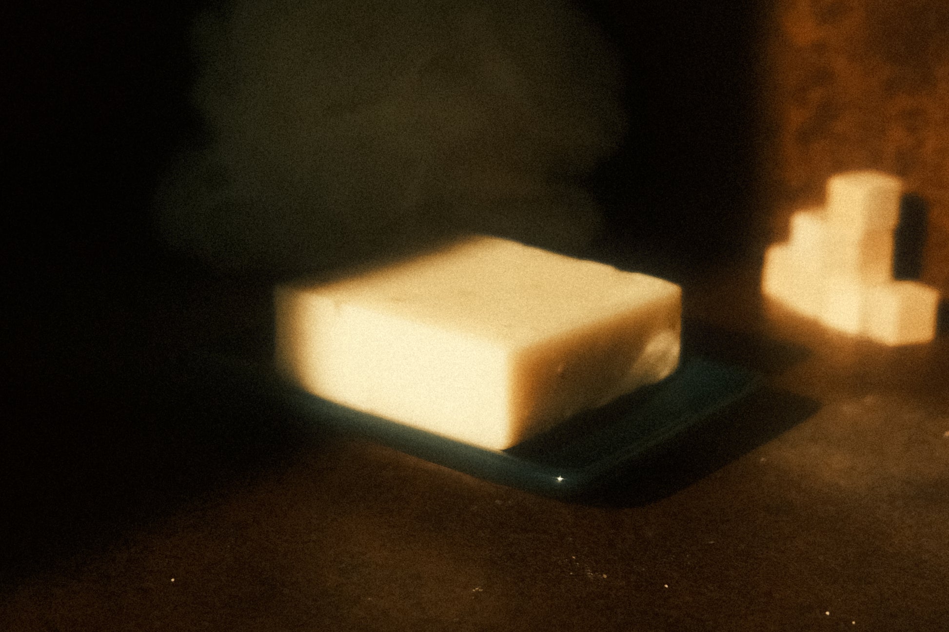 A white bar of soap on navy blue soap dish with a stack of cubes sitting in the background