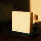 White bar of soap stands on navy blue soap dish with brown floor and beige background