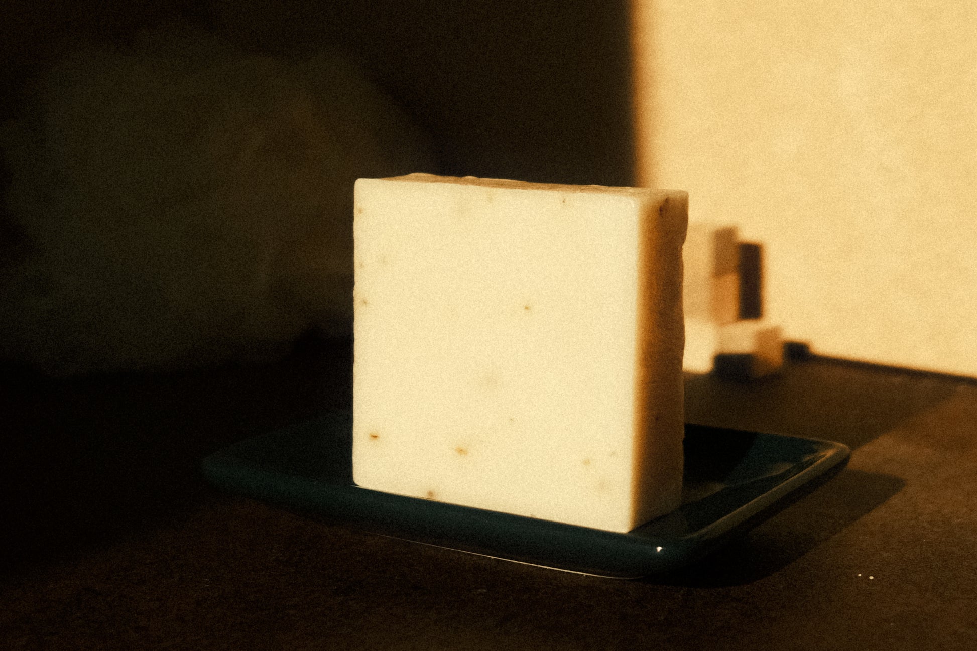 White bar of soap stands on navy blue soap dish with brown floor and beige background