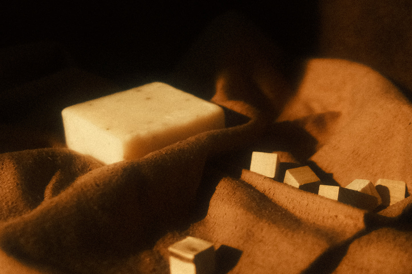 White bar of soap lays on brown cloth along with small cubes 