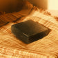 Black bar of soap laying flat on a plaid cloth