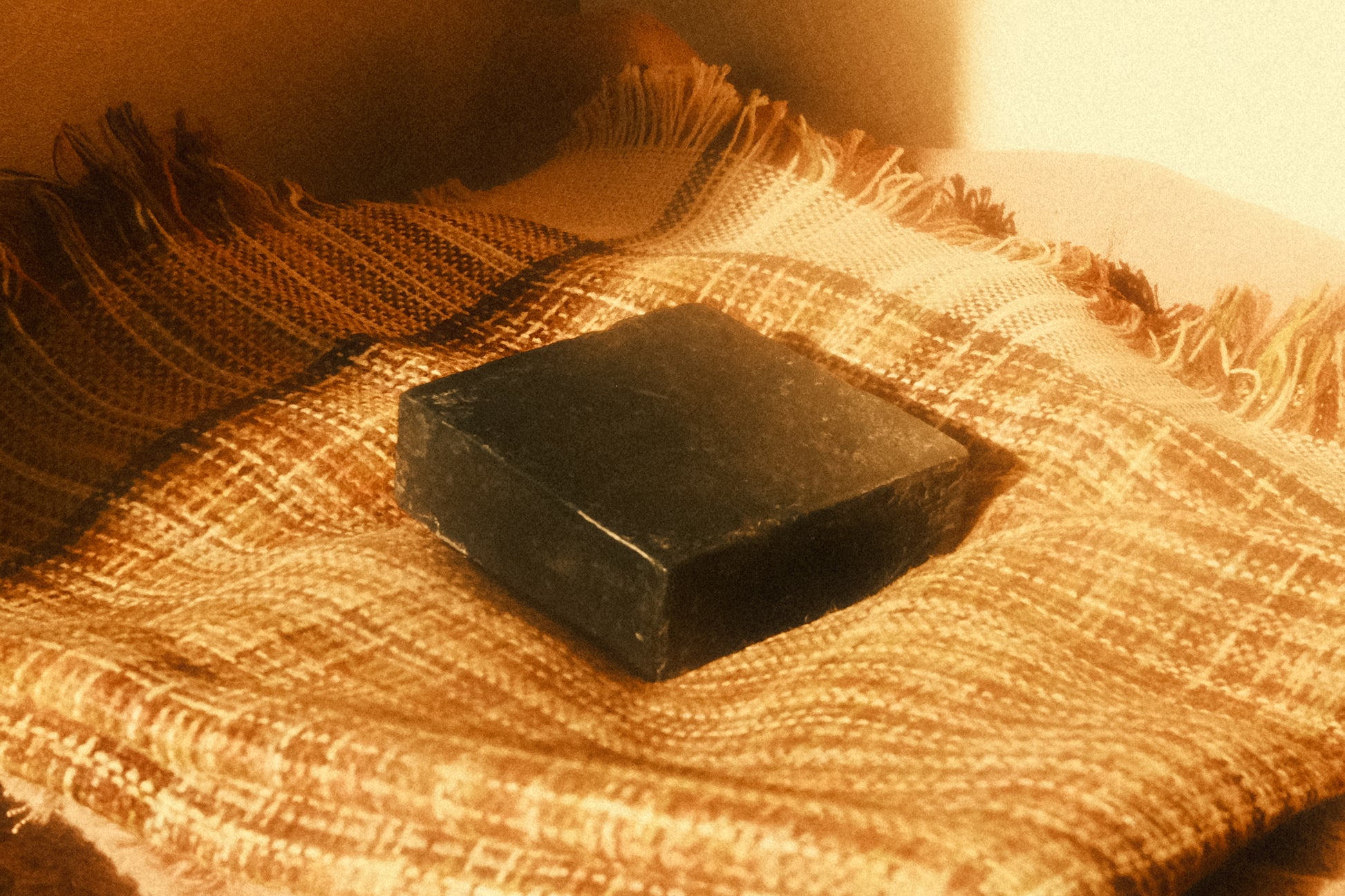 Black bar of soap laying flat on a plaid cloth