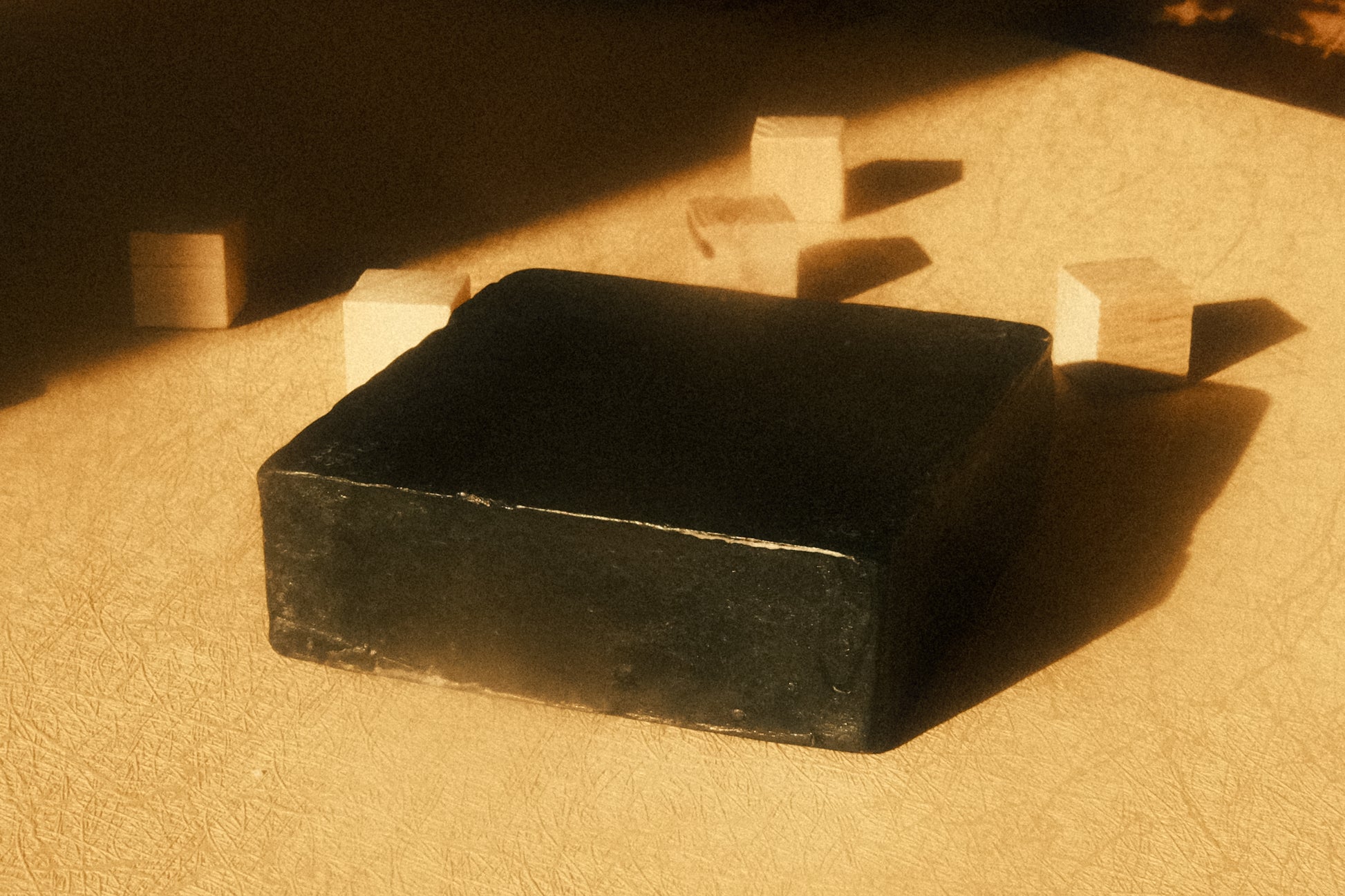 Black bar of soap laying flat on beige floor with small cubes behind it