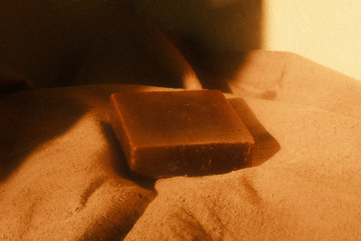 Brown bar of soap laying flat on beige cloth, a third of the photo within a shadow