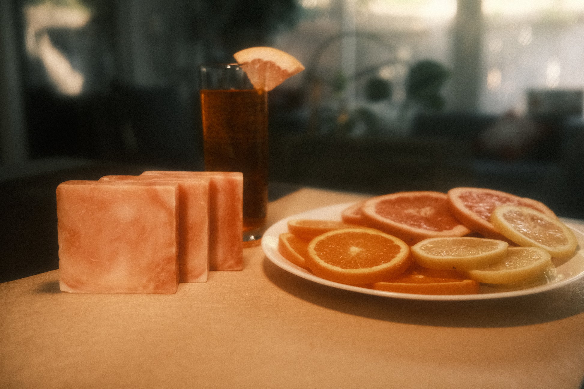 Orange swirled bars of soap on table with orange drink in background and orange slices on place to the right