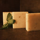 Three bars of white soap stand in ascending order with mint leaves garnishing the side, brown background and floor