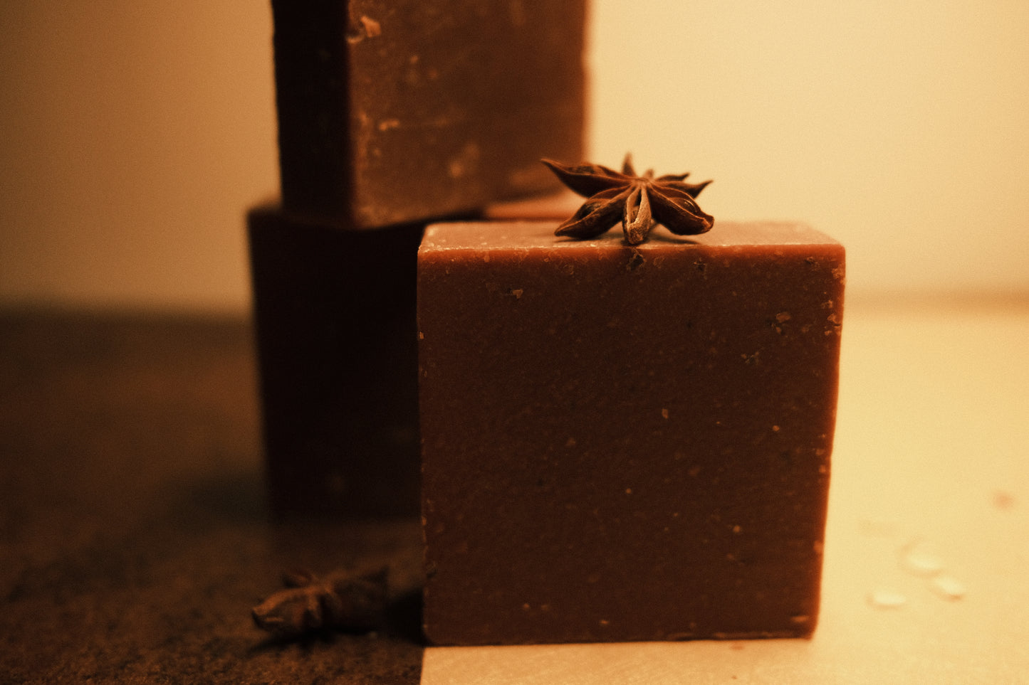 Three bars of brown soap, two stacked in the back and one standing in the front with a half brown and half beige floor. Garnished with star anise