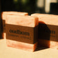 Three bars of marbled orange soap with brown labels, “oudbom, coastal citrus”